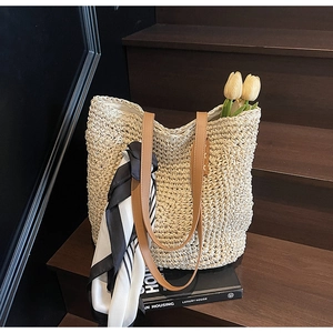 Detail of a beige woven straw tote bag with brown leather handles and striped silk scarf