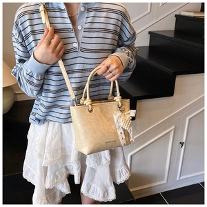 Close-up of cream textured bucket bag with pearl lace bow charm and adjustable strap