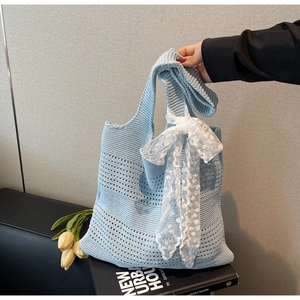Détail de la texture en tricot d'un sac cabas bleu clair avec un nœud en dentelle blanche
