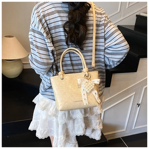 Detail of beige leather bucket bag with lace bow and pearl heart charm accessory