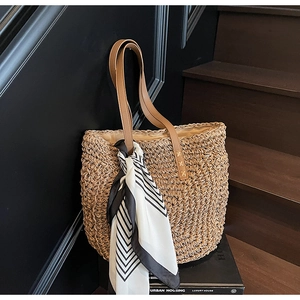 Detail of hand-woven straw tote bag with leather straps and decorative scarf on stairs