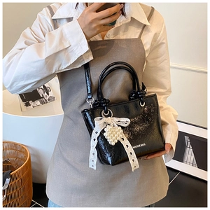 Detail of black glossy wrinkled leather mini bucket bag with lace bow and pearl charm