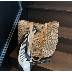 Detail of hand-woven straw tote bag with brown leather straps and geometric scarf