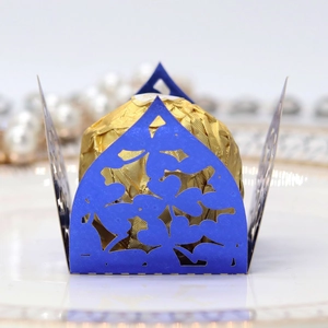 Macro view of blue laser-cut floral candy wrapper with a gold chocolate truffle inside