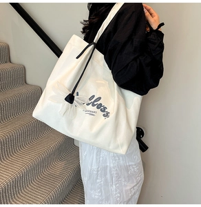 Detail of a large white canvas tote bag with black straps and a decorative mesh flower