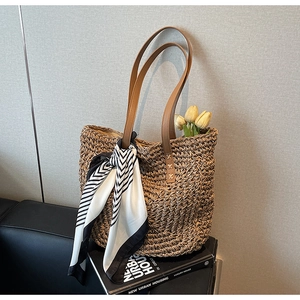 Detail of woven straw tote bag with brown leather handles and striped silk scarf accessory