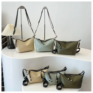 Three nylon dumpling bags in beige, mint, and olive on a minimalist display stand