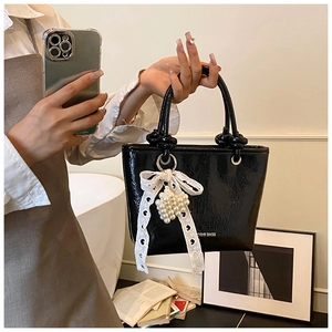 Detail of black glossy tote bag with white lace bow and pearl charm ornament