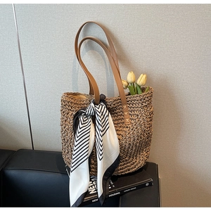 Detail of hand-woven khaki straw tote bag with leather handles and decorative silk scarf