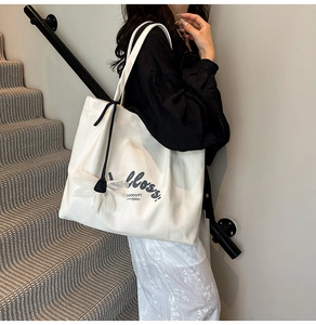 Detail of a white canvas tote bag with flossy lettering and a delicate flower pendant