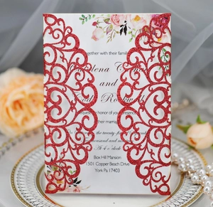 Close-up of red glitter laser-cut wedding invitation with floral printed insert card