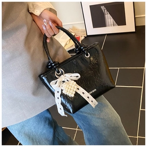Detail of black patent leather bucket bag with white lace bow and pearl decoration