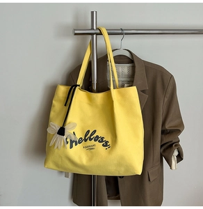 Detail of yellow canvas tote bag with black lettering and daisy flower charm detail