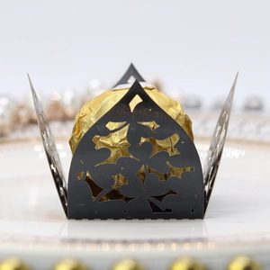 Close-up of laser-cut black floral chocolate wrapper with golden candy on a white plate
