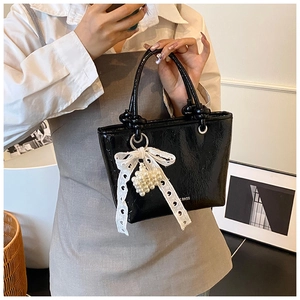 Close-up of black patent leather bucket bag with lace bow and pearl charm details