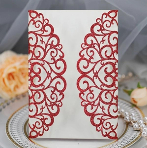 Detail of laser-cut wedding invitation with red glitter swirl patterns and cream cardstock