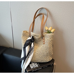 Close-up of straw tote bag with brown leather handles and striped silk scarf detail