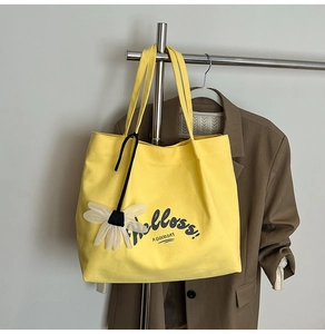 Detail of yellow canvas tote bag with Helloss print and daisy charm on a hanger