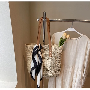 Detail view of woven straw tote bag with brown leather straps and striped silk scarf decor