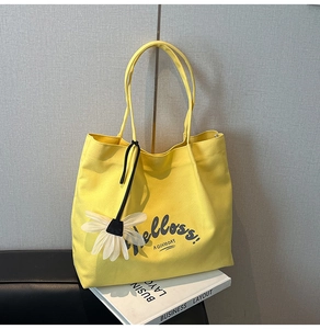 Detail view of yellow canvas tote bag with daisy pendant and black slogan print