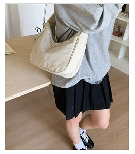 Détail du sac bandoulière en nylon beige avec poche latérale porté par le modèle