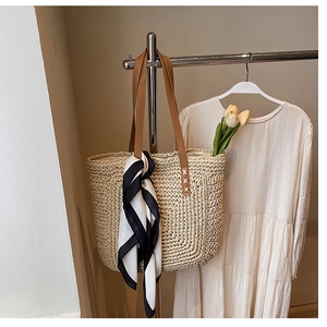 Detail of straw tote bag with brown leather handles and geometric scarf on hanger