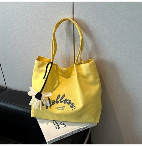 Detail of yellow canvas tote bag featuring floral pendant and black slim shoulder straps