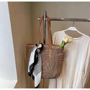 Detail of hand-woven straw tote bag with brown leather straps and decorative scarf accessory