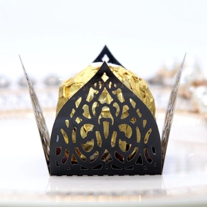 Macro shot of black laser-cut lace candy box with gold foil chocolate on white plate