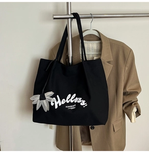 Detail of black canvas tote bag with Hello print and a white floral charm accessory