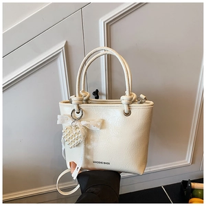 Detail of cream white pleated bucket bag featuring pearl heart charm and round handles