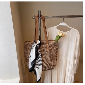 Close-up of woven straw tote bag featuring leather handles and a striped silk scarf detail