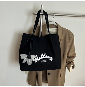 Detail of large black canvas tote bag with Helloss print and white petal charm accessory