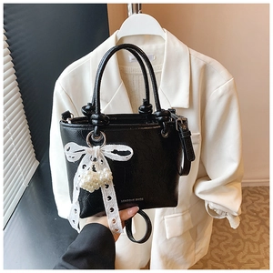 Detail of black glossy bucket bag with white lace bow and heart pearl pendant