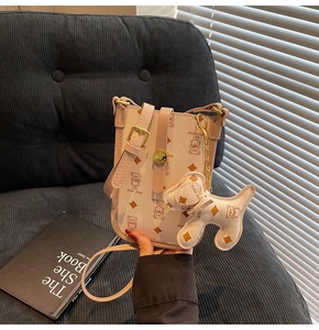 Detail of cream crossbody phone bag with teddy bear pattern and dog charm on sofa