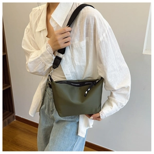 Detail of olive green crossbody bag featuring branded zipper pull and black wide strap