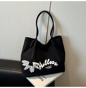 Detail of black canvas tote bag with Helloss print and white 3D flower charm