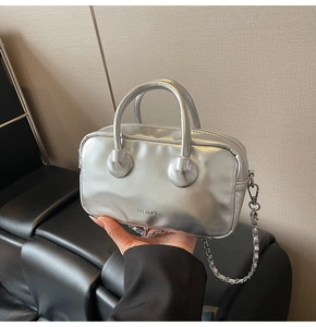 Detail of silver metallic bowling bag featuring dual handles and polished chain strap