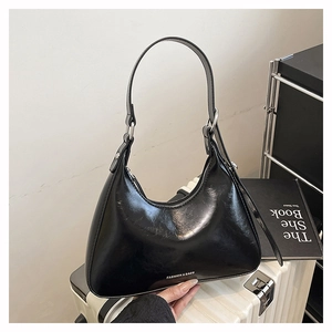 Detail of black glossy leather hobo bag with silver zipper on a white suitcase