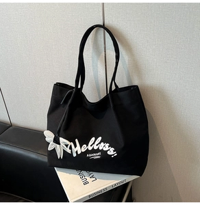 Detail of black canvas tote bag with white Hellos lettering and floral charm decoration