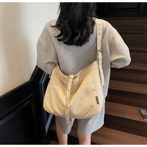 Detail of beige canvas tote bag with decorative eyelet strap and side logo label
