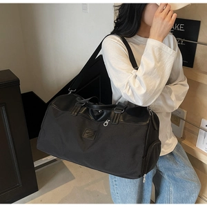 Model wearing large black travel bag with side zipper compartment and leather handles