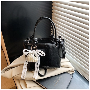 Close-up of black patent leather bucket bag with white lace bow and pearl heart charm