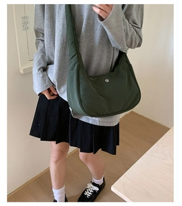 Détail d'un sac bandoulière demi-lune en nylon vert foncé avec une large sangle sur modèle
