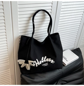 Close-up of black canvas tote bag with white floral pendant and text on a leather surface