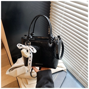 Detail of black pleated patent leather handbag with lace bow and pearl heart charm