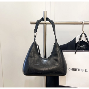 Detail of minimalist black crocodile pattern shoulder bag on a metal display stand