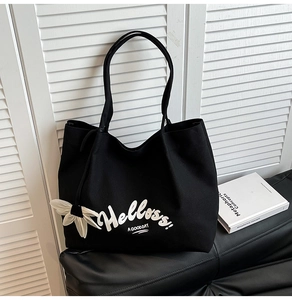 Detail of large black canvas tote bag with Helloss print and flower pendant on leather bench