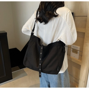 Detail of black canvas tote bag showing wide shoulder strap with silver metal eyelets