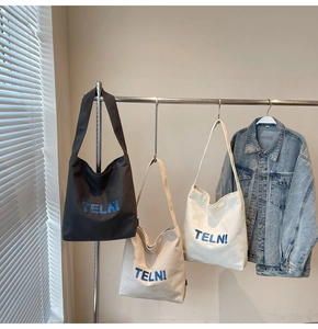 Dettaglio di borse tote in tela bianca e nera con ricamo blu TELN! su una gruccia